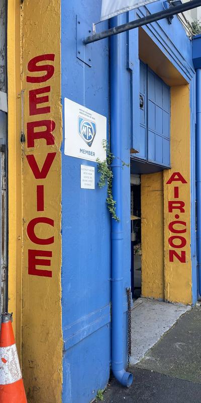 Painted signage on the Bourke Street frontage reading Service, Air-Con, Suspension and Exhaust, beside the MTA member plaque